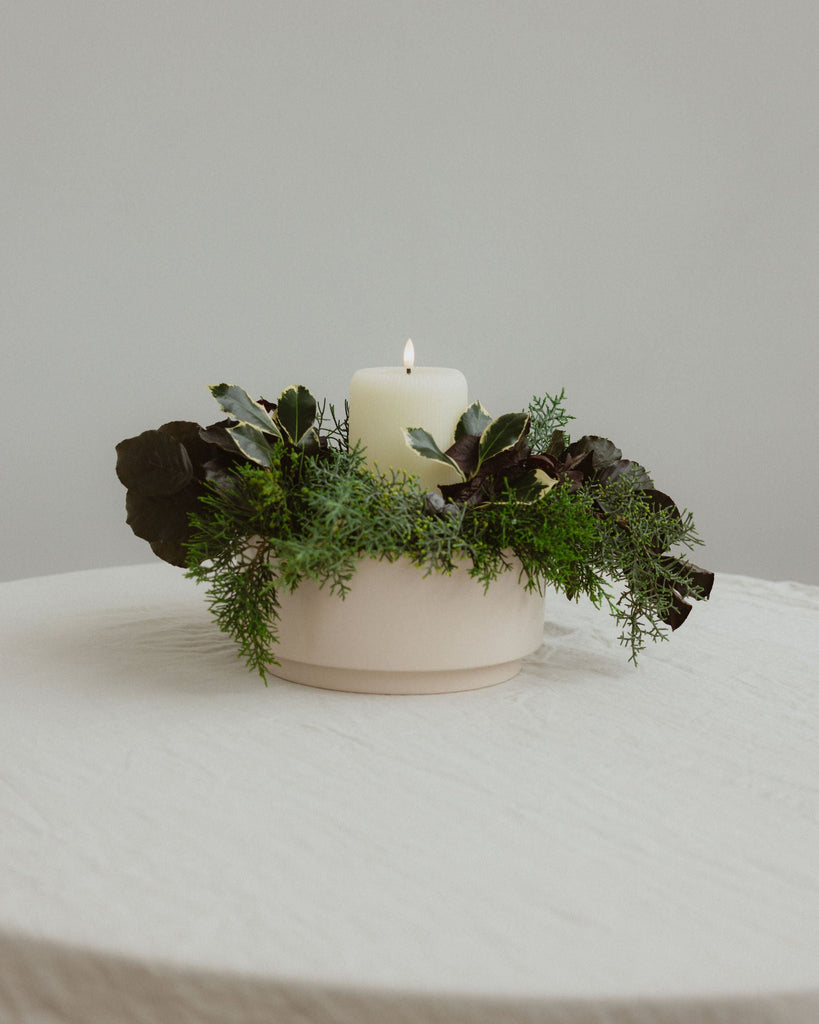 Decorative candle with greenery on a white surface against a plain background