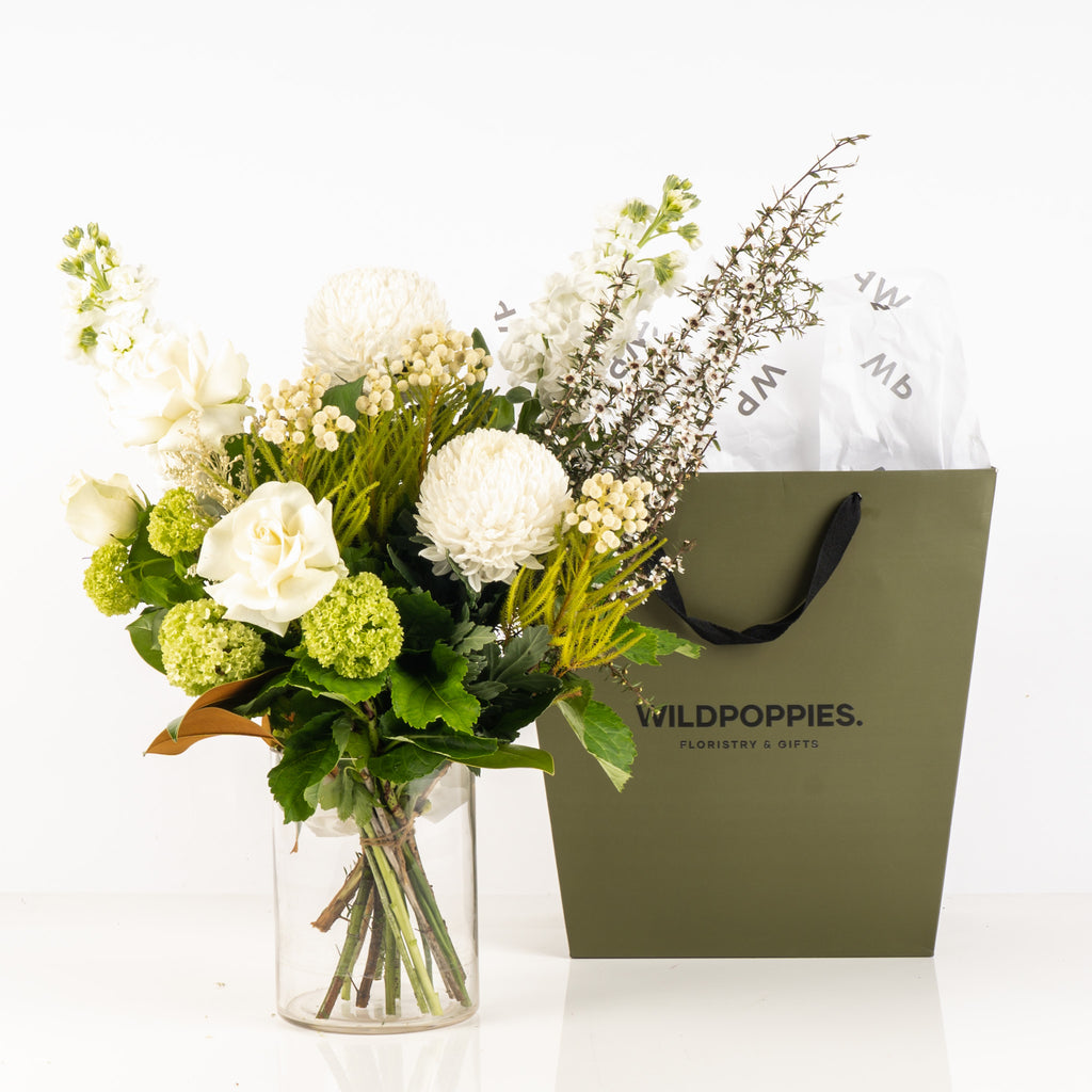 Fresh Whites n Greens Flower Subscription by Wild Poppies displayed in a glass vase beside a branded gift bag, ideal for elegant floral gifting.