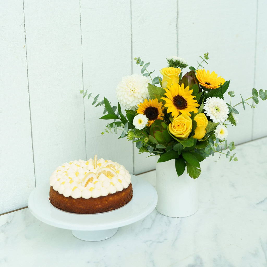 Lemon Curd Posy Cake Gift with fresh sunflowers and roses in a white vase beside a lemon curd cake, perfect for special occasions.