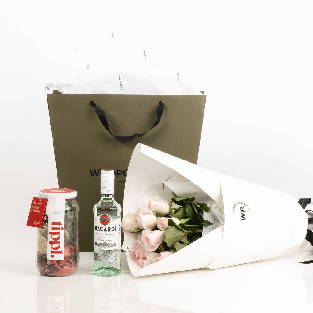 Blush & Bacardi Gift Set featuring a bouquet of pale pink roses, a Bacardi rum bottle, and cocktail mix, ideal for romantic celebrations.