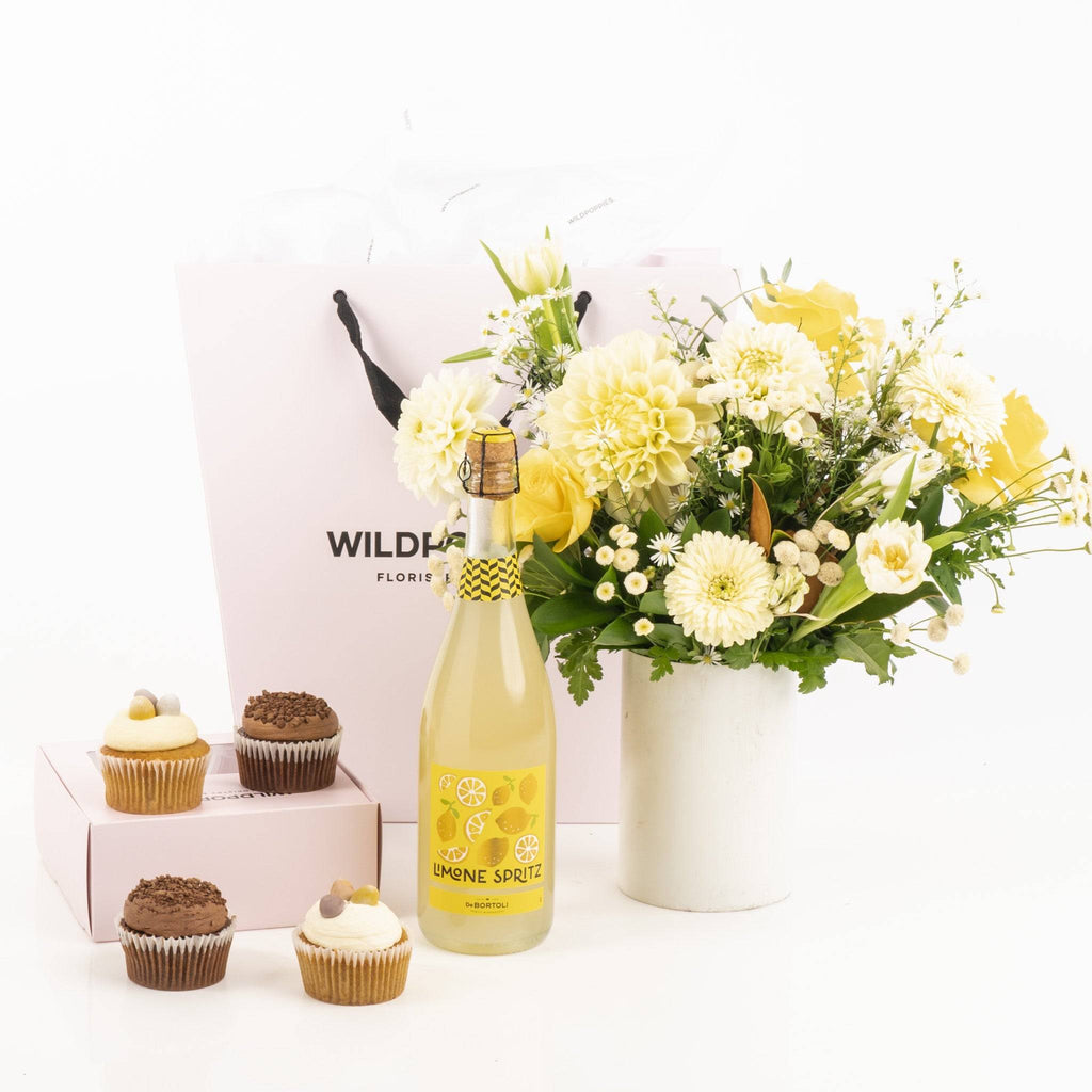 Limone Spritz Easter Gift Set featuring a bottle of Limone Spritz, yellow and white floral posy, and festive cupcakes in a gift bag. Ideal for stylish celebrations.