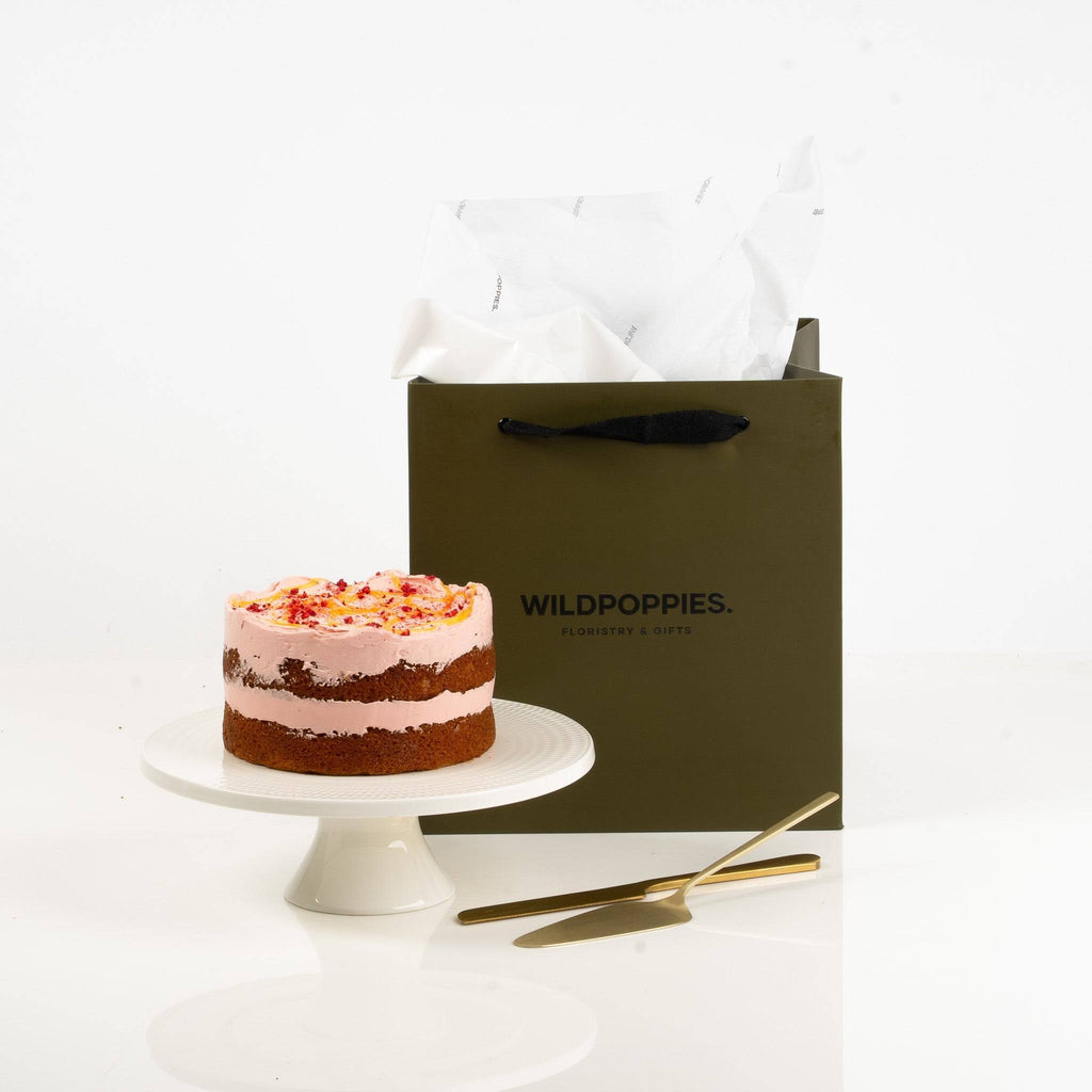 Small cake on a white stand next to a green 'Wildpoppies' gift bag on a white background