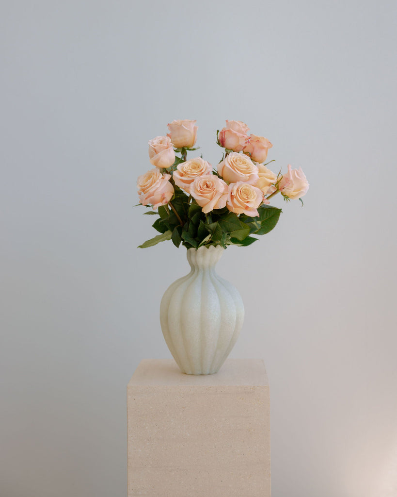 Bouquet of pink roses in a white vase on a beige pedestal against a light gray background